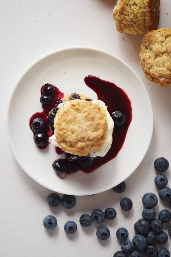 Overhead photo of blueberry shortcake on a white plate with fresh blueberries