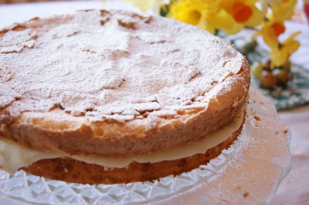 gluten free lemon cake, covered in icing sugar with daffodils in the background