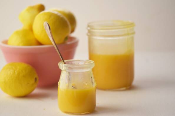 two jars of lemon curd with a pink bowl of lemons in the background