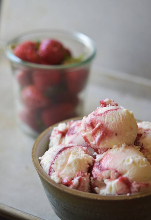 strawberry swirl ice cream in a bowl with strawberries in the background