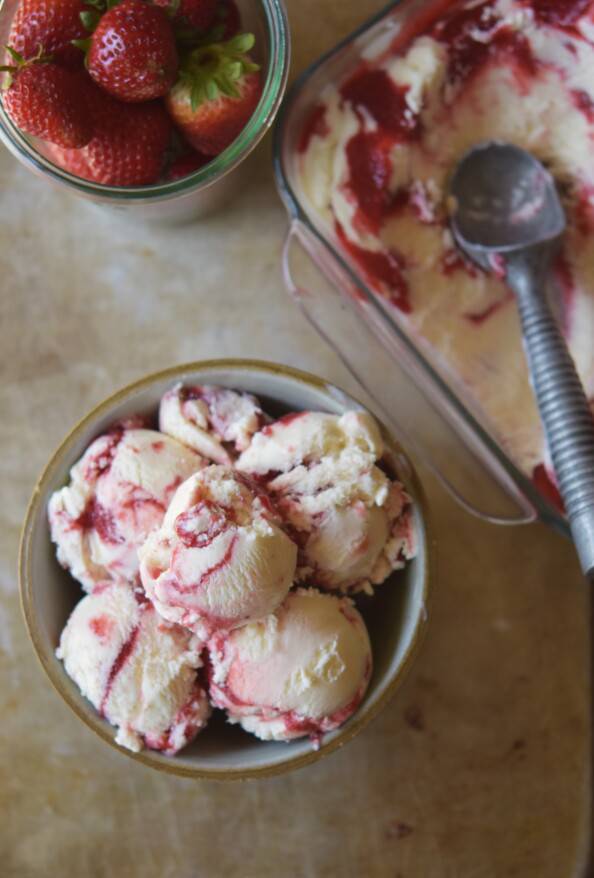 overhead of new york cheesecake ice cream in bowl with scoop and berries