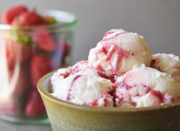 close up of strawberry swirl cheesecake ice cream with berries in the background