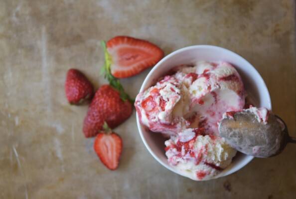 strawberry cheesecake ice cream in white bowl with cut berries