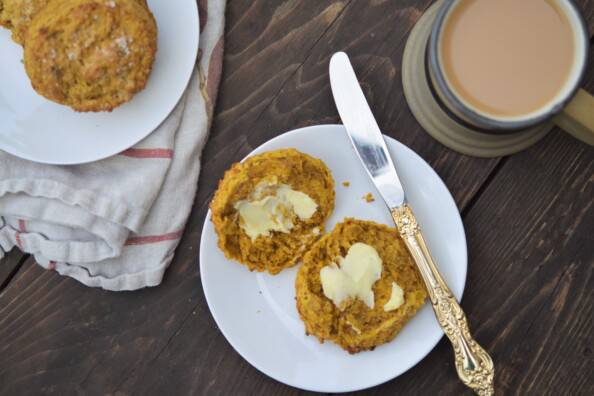 overhead photo of pumpkin scone on a white plate with a cup of tea on a wooden table