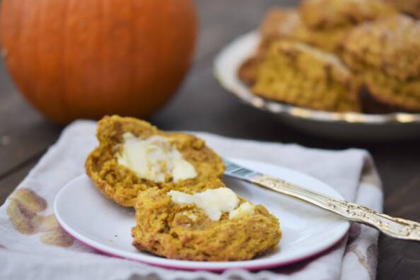 pumpkin spice scone, split open and buttered on a white plate with a pumpkin in the background