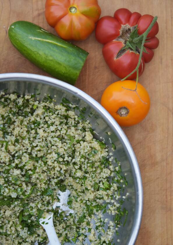 overhead photo of a metal bowl with quinoa and herbs with tomatoes and cucumbers beside it