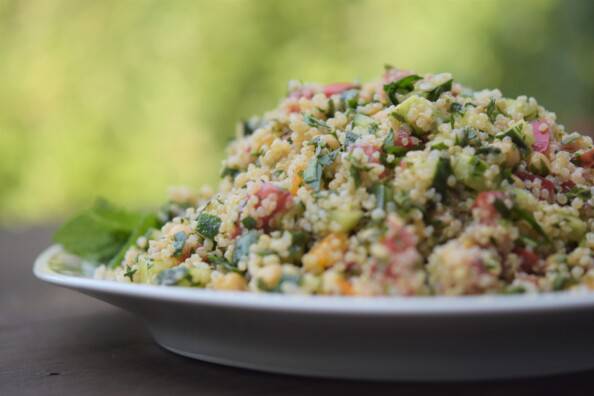 a mound of quinoa tabbouli salad on a white platter with a blurred green background