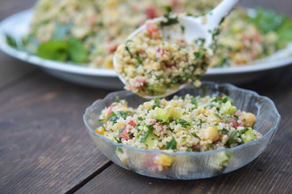 spooning quinoa tabbouleh from the platter to the bowl, on a wooden table