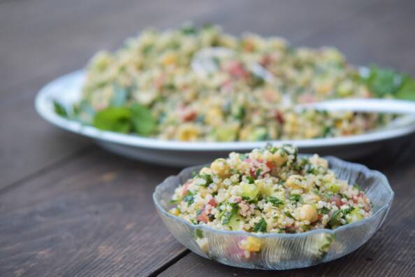 a bowl of tabbouli salad on a wooden table with a serving platter behind